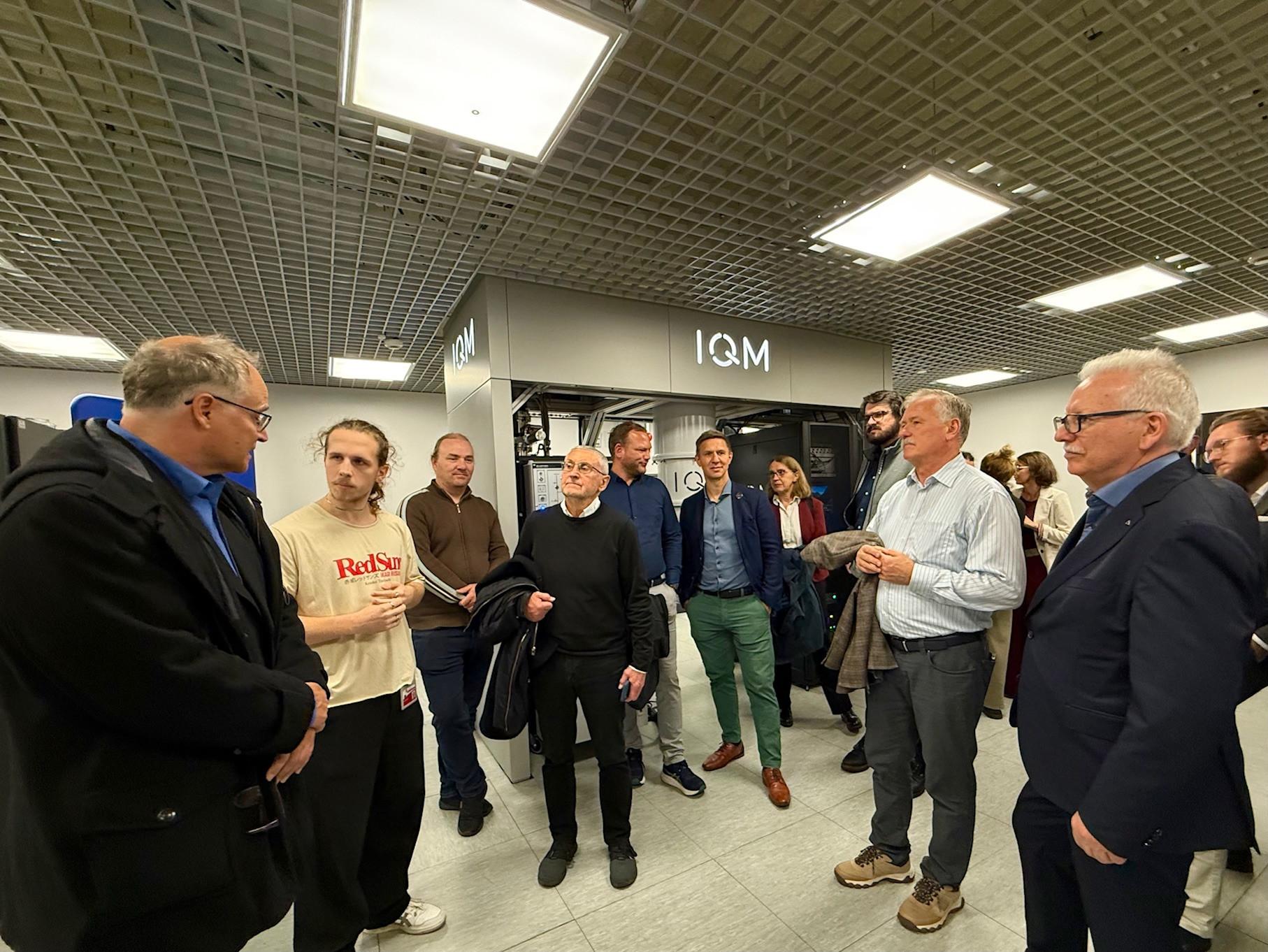 Besuch im Quantenlabor der TU Wrocław. Eine Gruppe von Personen steht in einem Technikraum und hört einer erklärenden Person zu. Im Hintergrund ist ein Quantencomputer zu sehen.