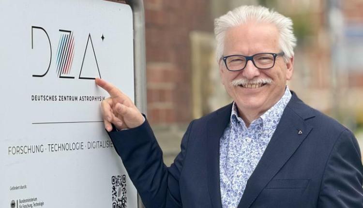 Ein Mann mit Brille steht neben einer hellen Tafel mit der Aufschrift DZA und zeigt mit der Hand darauf.